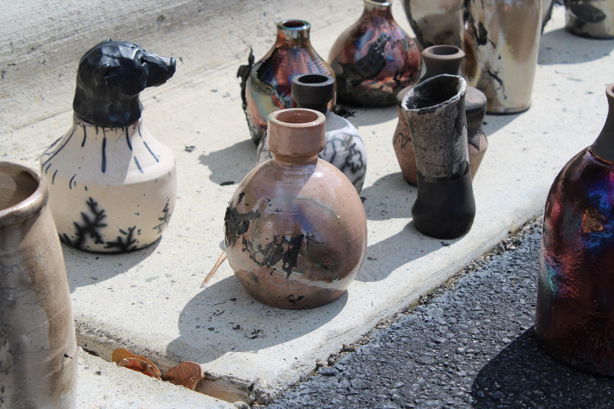 A variety of finished raku pieces cooling off on the ground.