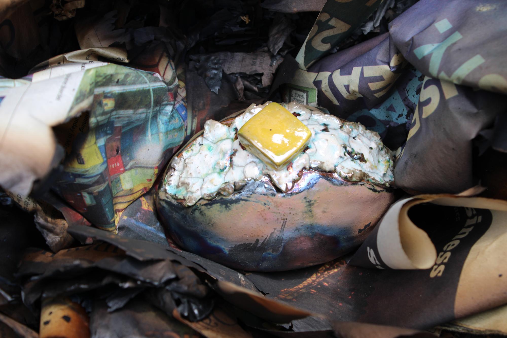 Raku fired piece of pottery that looks like a baked potato cut open with a pad of butter.