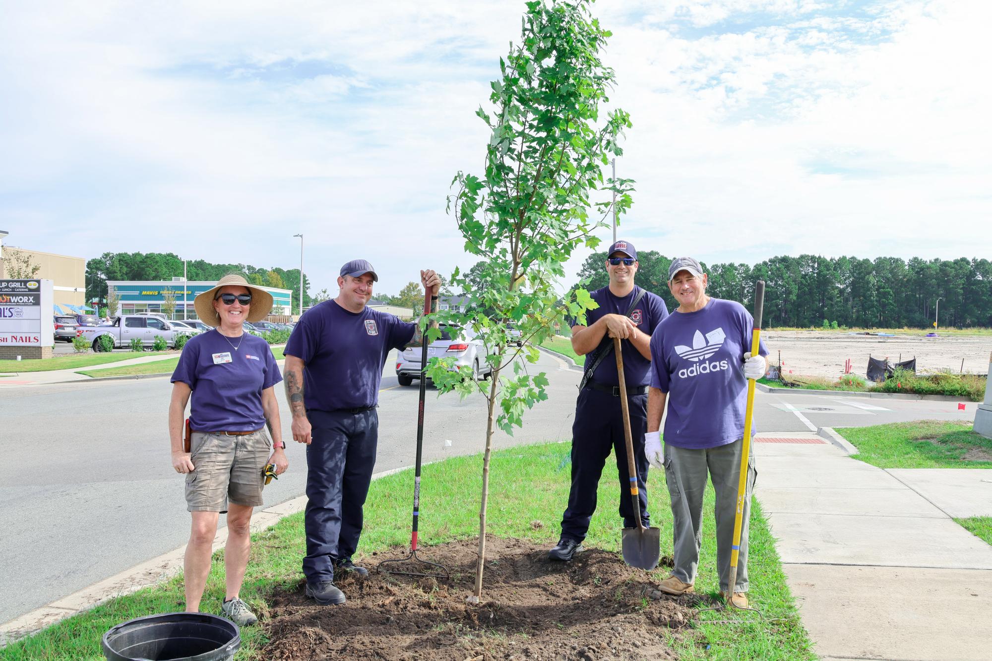 Four people standing beside a planted tree