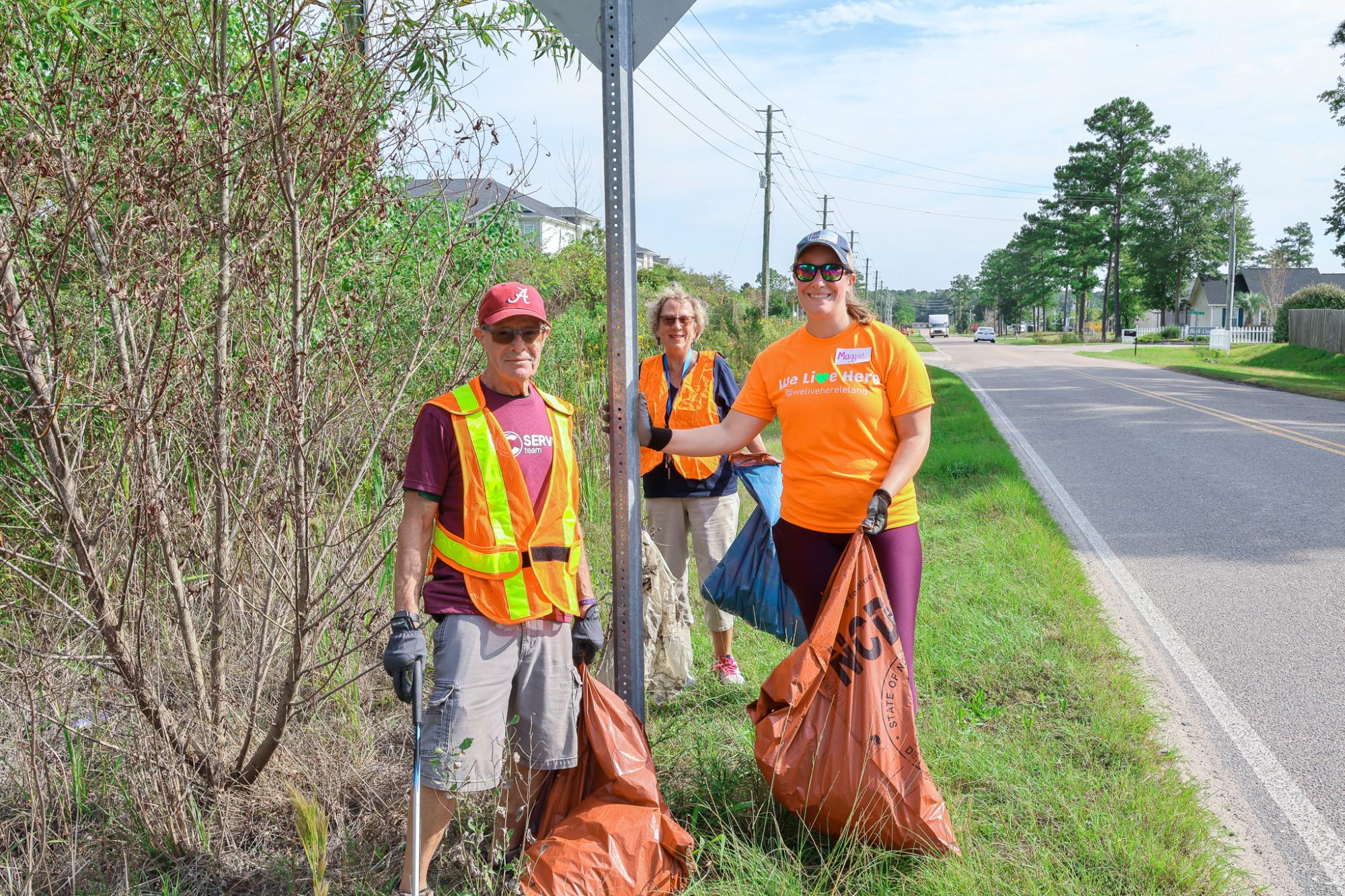 Three people standing beside the road holding trash bags