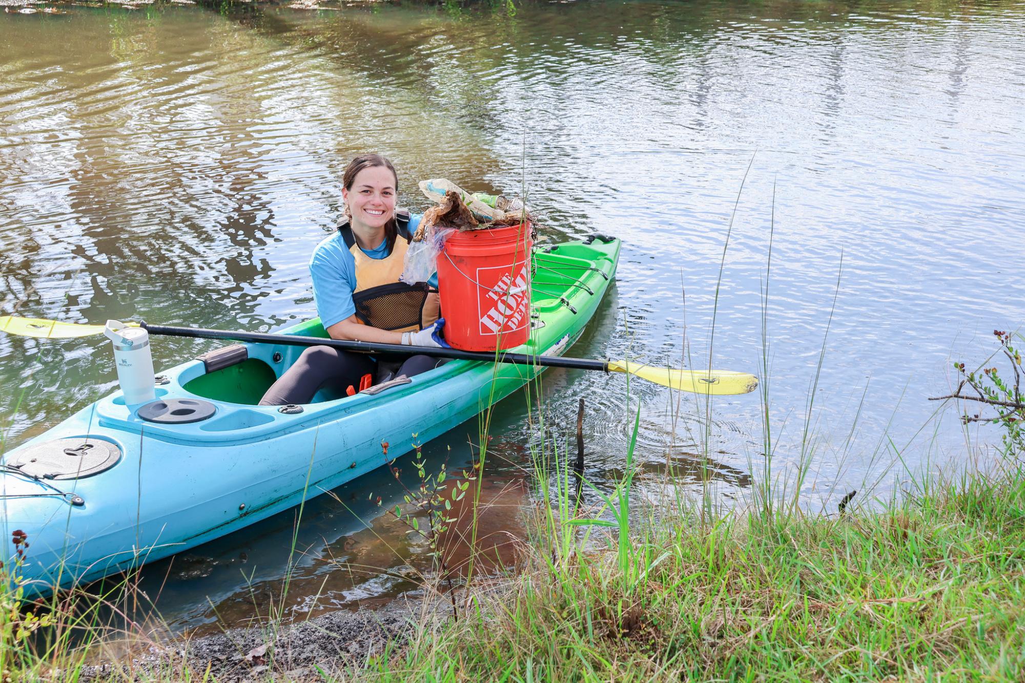 One person sitting in a kayak holding a bucket of collected trash