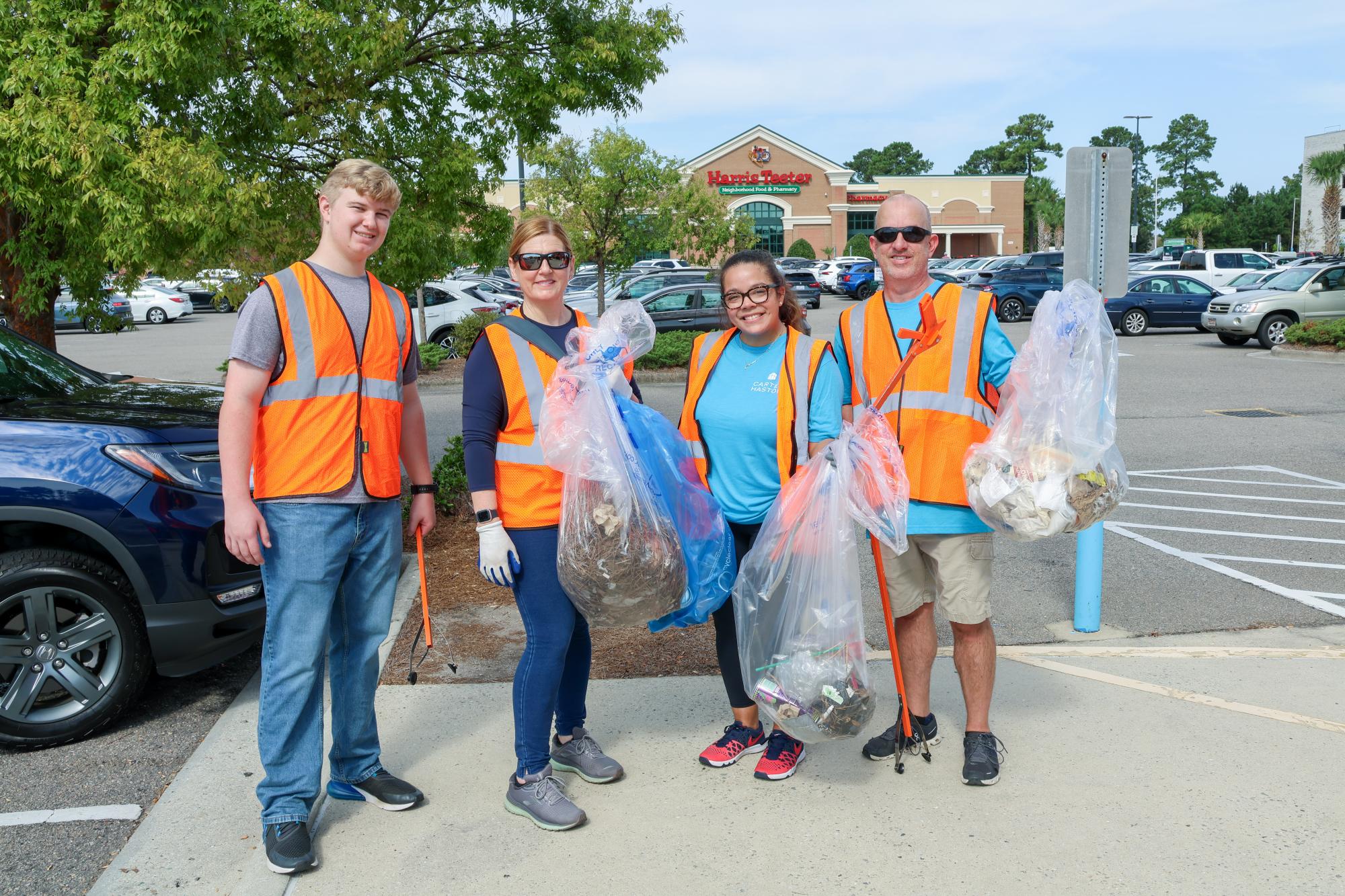 Four people standing side by side holding trash bags